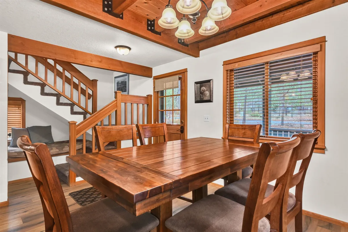 A warm dining area with a wooden table, a glowing chandelier overhead, and a staircase in view. The space evokes a sense of togetherness and cozy evenings spent indoors.