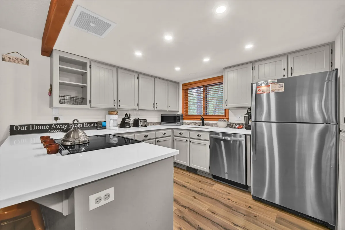 A bright, inviting kitchen scene with a prominent kitchen island, stainless steel appliances, and wooden window frames letting in natural light. The breakfast bar is set for casual dining, and the modern finishes—including quartz countertops—are evident.