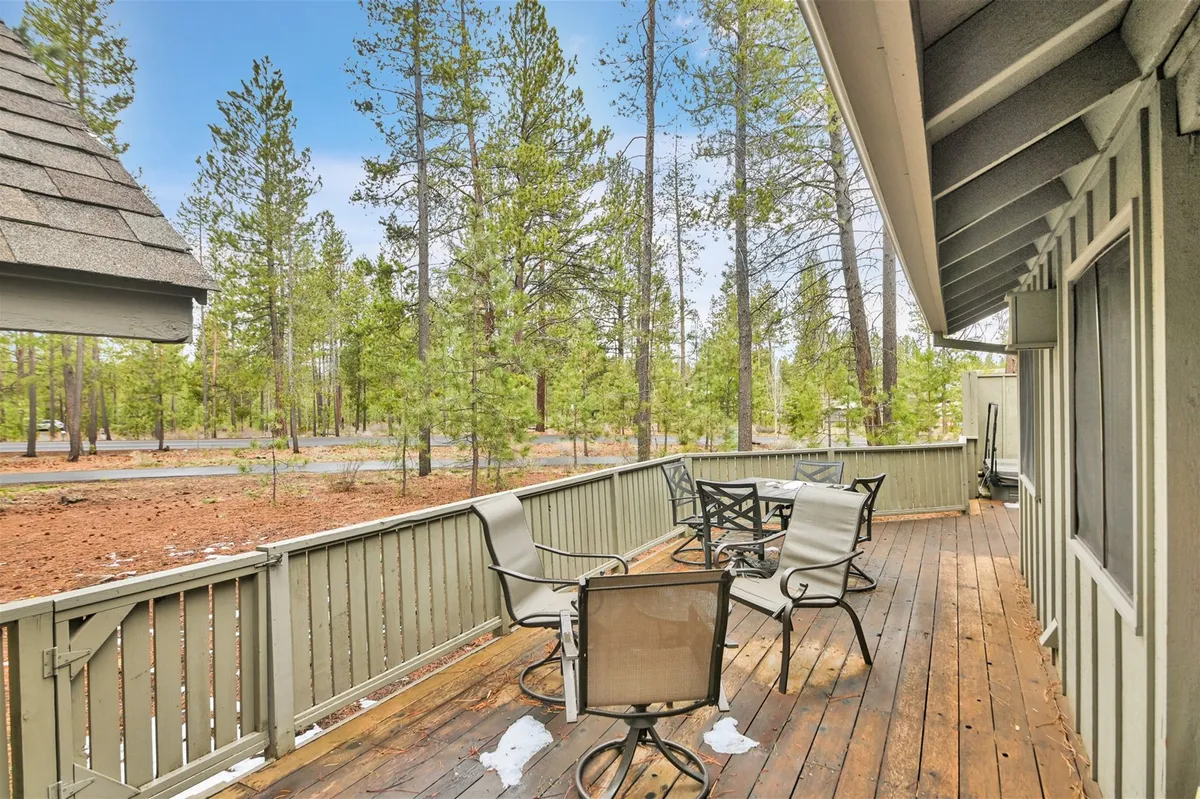 This shot offers a close view of the outdoor seating arrangement on a wooden deck nestled among tall trees. The peaceful atmosphere invites guests to enjoy meals outdoors, socialize, or simply appreciate the surrounding natural beauty at any time of day.