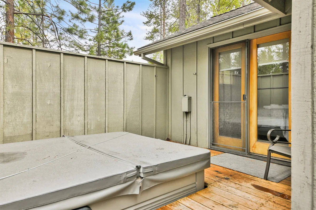 The image displays a tranquil hot tub set on a wooden deck, just outside the home and adjacent to a sliding glass door. The setting suggests serenity, with ample space for relaxing and soaking under the stars, directly linking the indoor and outdoor experiences.