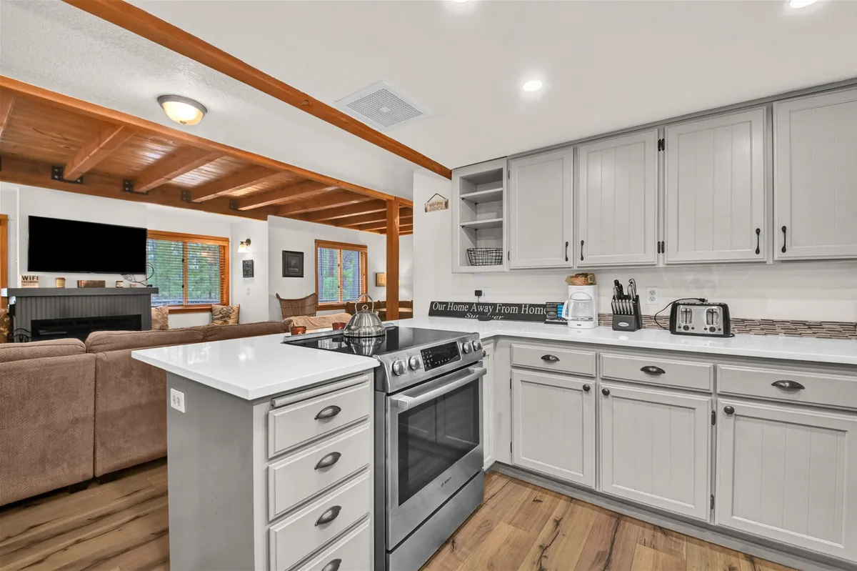 This image features the inviting kitchen island, a sleek stainless steel stove, and an open living area—all styled to feel cozy and welcoming. The space is ideal for cooking, gathering with friends or family, and entertaining, reflecting a blend of functionality and comfort that supports both work and leisure.