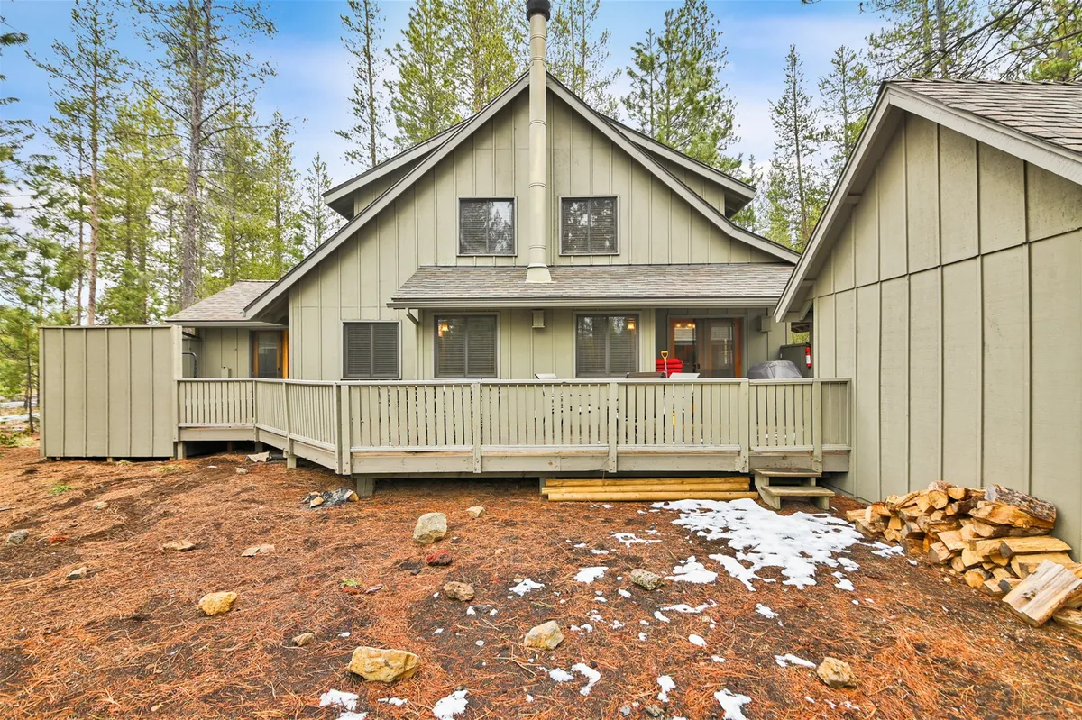 This image beautifully showcases the home's spacious wooden deck surrounded by mature trees, with a chimney and a welcoming stack of firewood. The deck is designed for both outdoor gatherings and quiet moments, offering a prime spot for grilling or relaxing as the sun sets, all immersed in a peaceful natural setting.