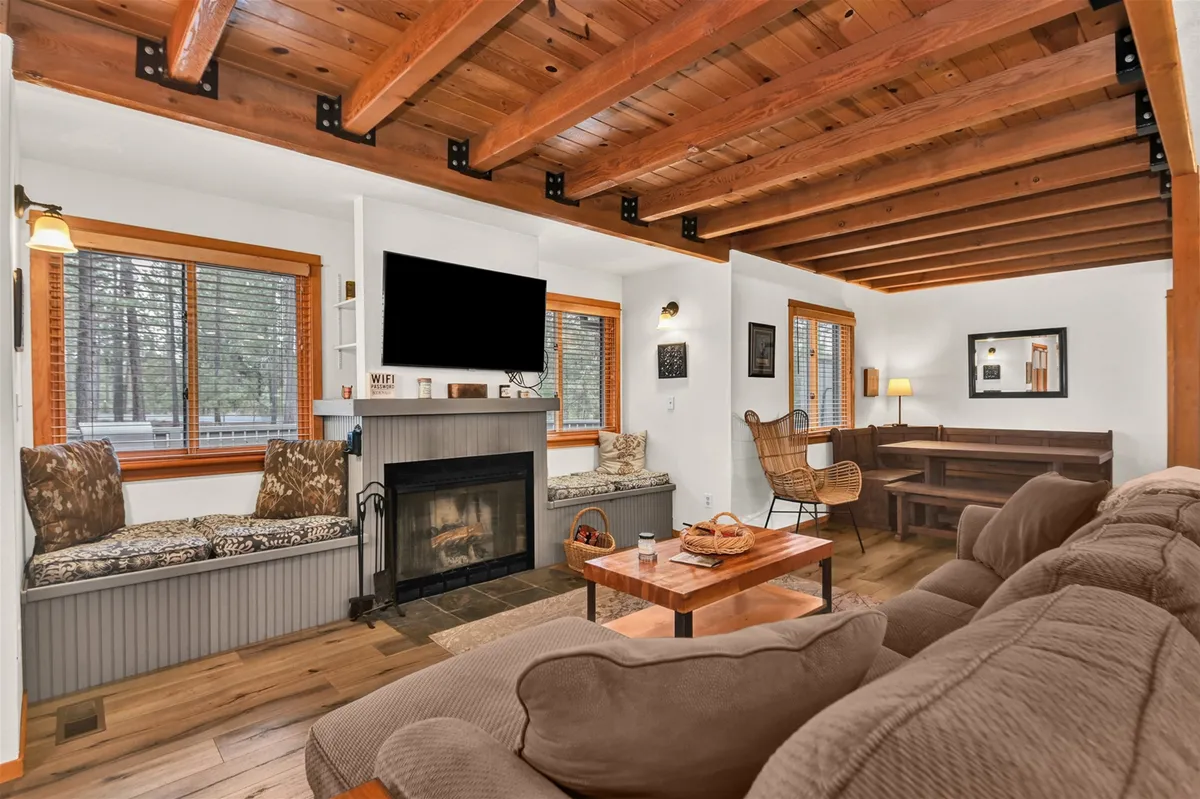 A spacious, inviting living area featuring a central wood fireplace, comfortable seating, a wooden dining table, and large windows that fill the room with natural light. The setting invites relaxation and family gatherings after a day of resort activities.