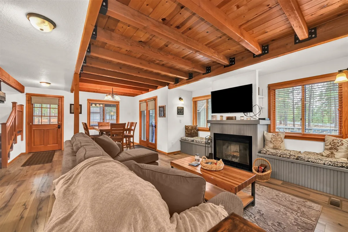 A cozy living and dining space with a plush sofa, a wood-burning fireplace, an inviting dining table, and window seating. The ambient setting is perfect for family gatherings, watching TV, or simply relaxing in a peaceful atmosphere.