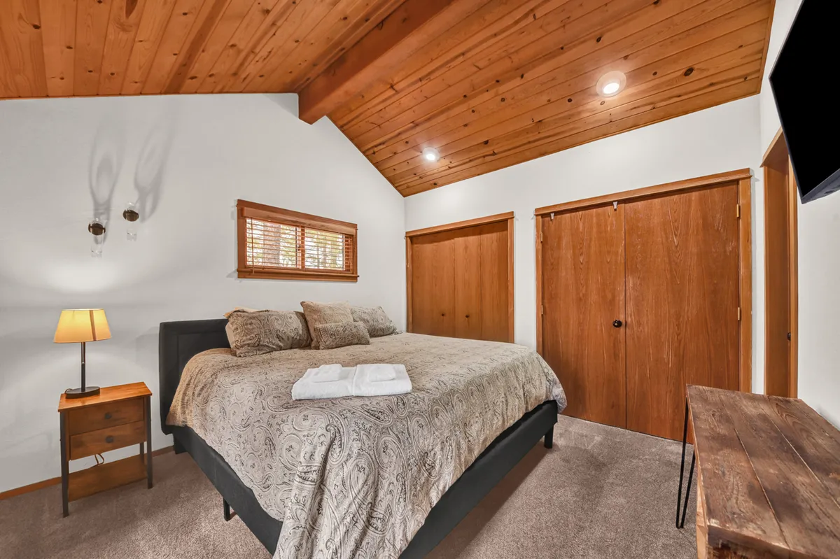 This photo captures a welcoming bedroom with a queen-sized bed, decorative pillows, a wooden bedside table with a lamp, textured walls, and wooden closet doors. The room exudes comfort and relaxation, ideal for unwinding after a day of activities.