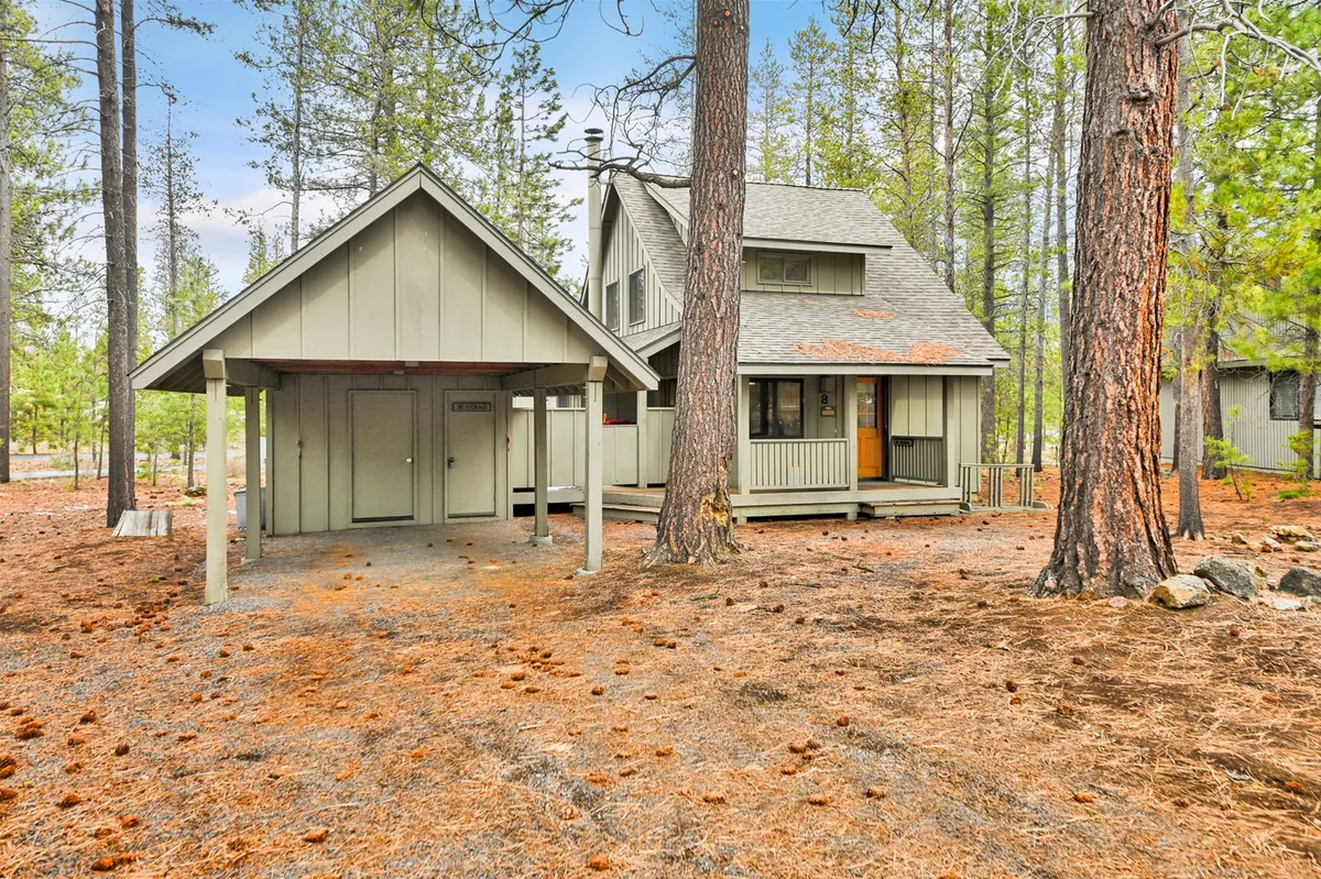 This image shows the welcoming front porch of the home framed by a peaked roof and surrounded by tall trees. A stone pathway winds up to the entrance, suggesting easy access to and from outdoor adventures in the Sunriver area.