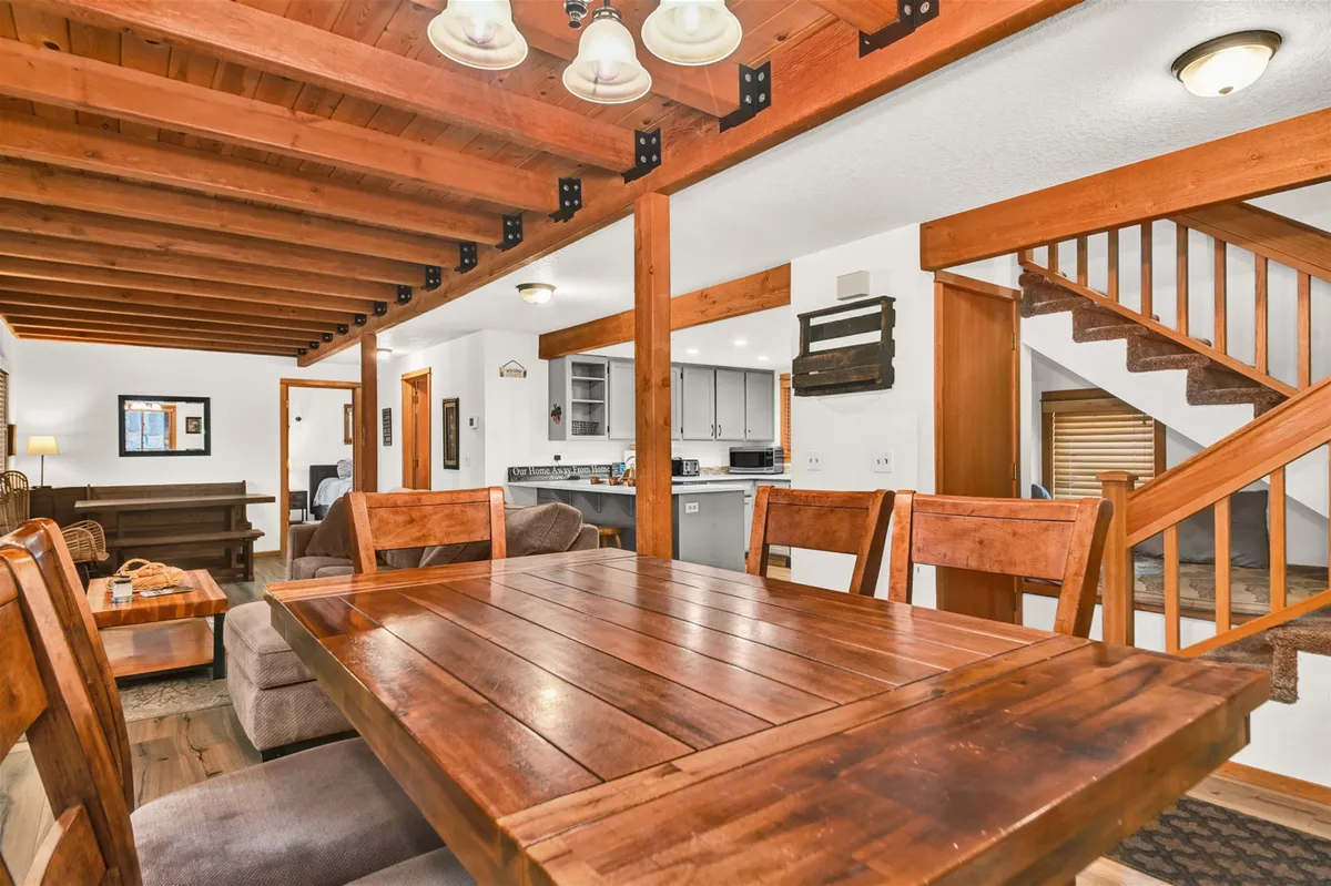 An open-plan kitchen and dining space with a wooden table, visible staircase, exposed beams, and a modern kitchen area. The environment is warm, inviting, and clearly designed for gatherings, celebrations, and family traditions, showcasing the heart of the home where cooking and socializing intertwine.